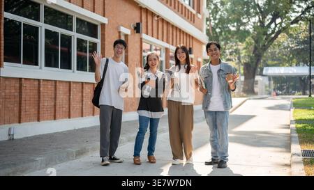 Group of Asian students waving hand standing together on walkway outside the building campus after classes during daytime Stock Photo
