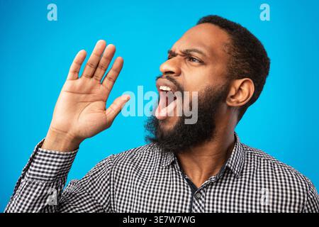 Black man looking away and shouting while standing against yellow background in studio Stock Photo