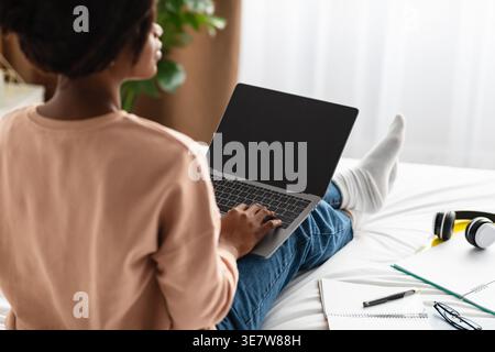 Back-View Of African American Woman Using Laptop With Blank Screen Typing And Browsing Internet Sitting In Bedroom At Home. Unrecognizable Female Free Stock Photo