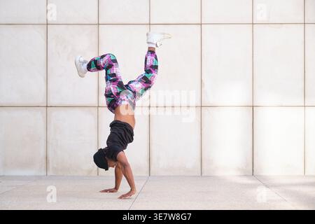 Mixed-race male dancer doing handstand with legs spread on street during daytime Stock Photo