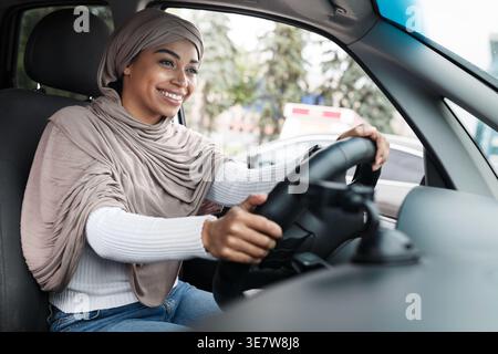 Cheerful Black woman in hijab driving car in city during daytime Stock Photo