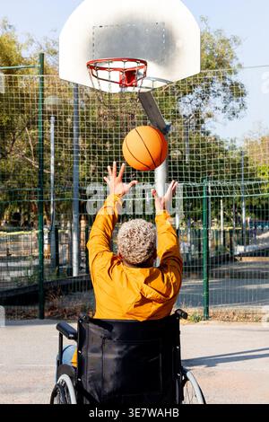 Disabled Hispanic man sitting in wheelchair playing basketball on basketball court on sunny day Stock Photo