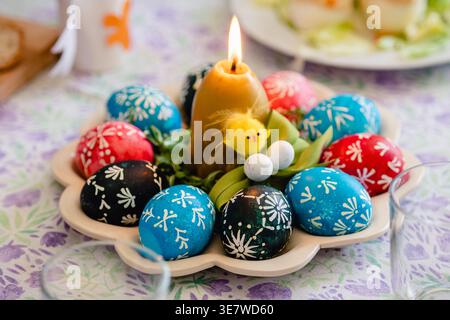 Lithuanian traditional Easter eggs painted with beeswax and natural colours,  in a tray with a candle on a decorated festive table Stock Photo
