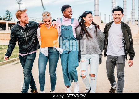 Cheerful group of diverse male and female friends walking together on city street during daytime Stock Photo
