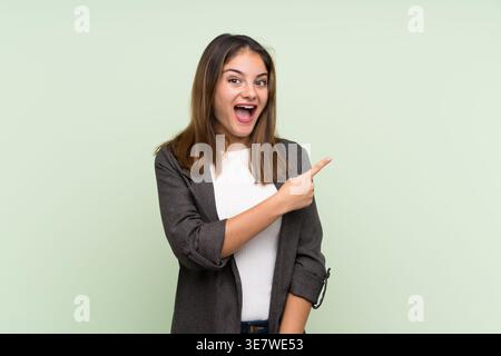 Surprised Hispanic woman wearing blazer pointing sideways standing against light light green background in studio Stock Photo