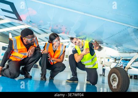 Diverse aircraft maintenance crews inspecting airplane fuselage while kneeling in hangar Stock Photo