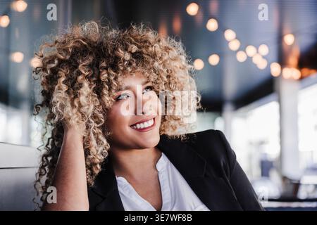 Hispanic female looking away touching curly hair sitting at table in cafe Stock Photo