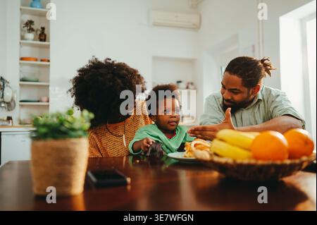 Smiling Black family having fun while sitting together at breakfast table at home Stock Photo