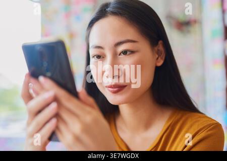 Asian woman using smartphone while sitting at table in cafe Stock Photo