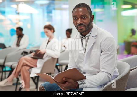 African American male medical student wearing lab coat holding notebook sitting in audience during medical seminar in conference room Stock Photo