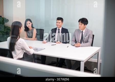Smiling Chinese woman sitting at table having a job interview with hr specialists in office Stock Photo