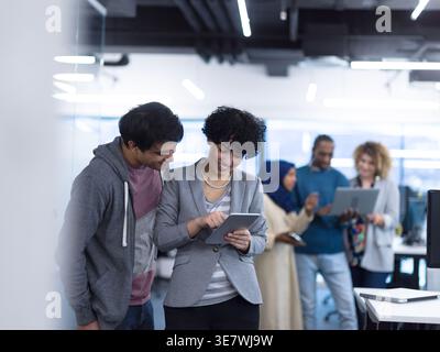 Mixed race male and female workmates working together on tablet standing in office Stock Photo