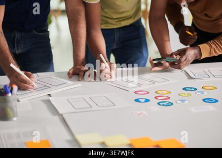 Group of Asian male designers holding smartphone leaning on table working together in office during daytime Stock Photo