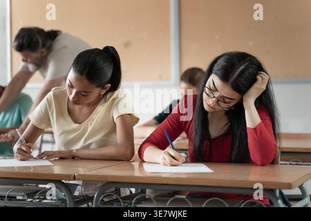 Focused Hispanic and caucasian female students sitting at desks and taking their exams in the classroom Stock Photo