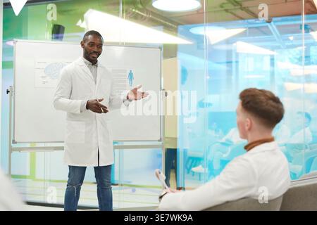 African American male college instructor standing near whiteboard in front of students giving presentation during medical seminar in conference room Stock Photo