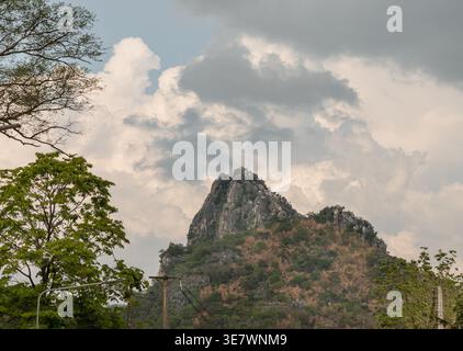A jagged limestone peak pierces the horizon, its weathered grey face rising in sharp contrast to the dense greenery below. Lush, sun-dappled trees fra Stock Photo