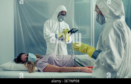 Black and Caucasian health workers with protection suits examining female patient in hospital Stock Photo