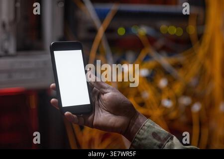 Black woman holding smartphone with blank screen standing near cables and wires in server room Stock Photo
