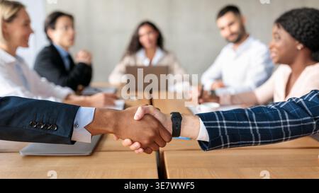 Cropped image of Black and caucasian male employees over table in front of colleagues in office Stock Photo