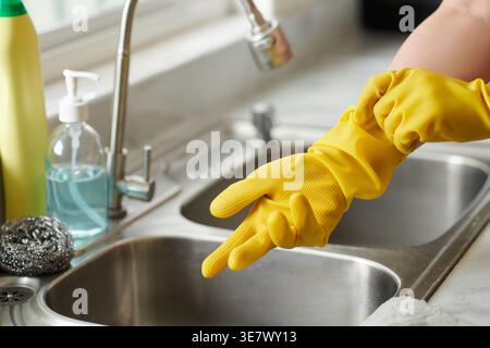 Asian woman putting on yellow gloves standing near kitchen sink in kitchen at home Stock Photo