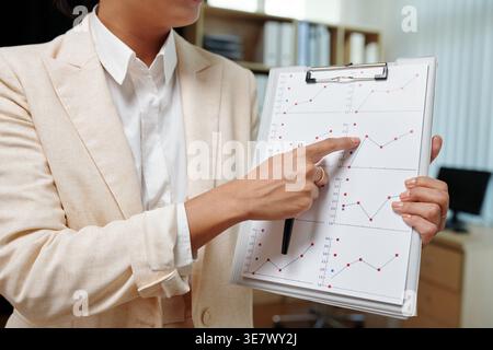 Mixed race business woman wearing suit pointing at chart while standing in office Stock Photo
