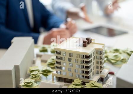 Cropped image of Asian and caucasian male architects discussing about architectural model and construction plans while sitting at table in office Stock Photo