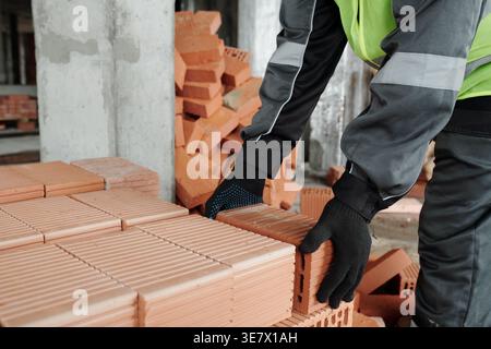 Black man worker hands wearing gloves putting bricks on stack in construction site during daytime Stock Photo