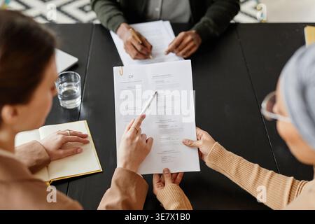 High angle of mixed race and caucasian female HR managers sitting at table and discussing resume of male candidate during job interview in office Stock Photo