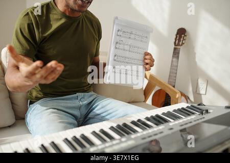 Black man showing music sheet sitting on sofa near piano in living room at home Stock Photo