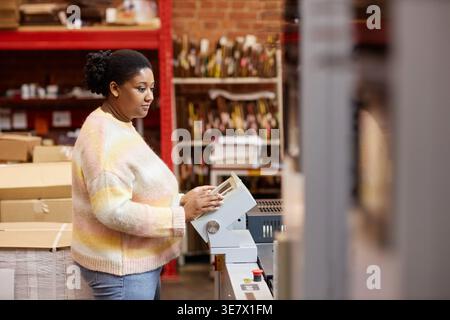 Black female worker operating industrial printing machine during work in printing shop Stock Photo