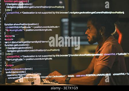 Indian male programmer examining computer codes sitting at table working late at night in office Stock Photo