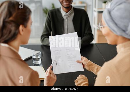 Mixed race and caucasian female HR managers sitting at table holding resume of male candidate during job interview in office Stock Photo