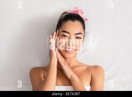 Asian woman touching face lying on bed in spa Stock Photo