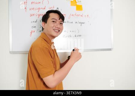 Asian male computer programmer standing against whiteboard with programming code in office Stock Photo