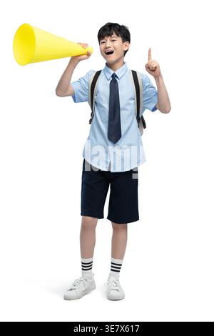 Chinese boy student shouting through megaphone while standing against white background in studio Stock Photo