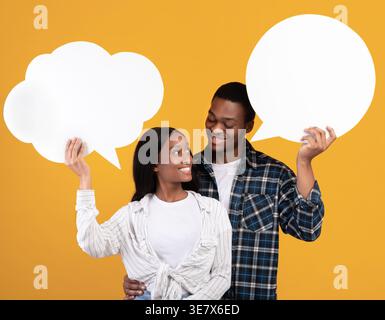 Black couple holding speech bubble cardboard while standing against yellow background in studio Stock Photo