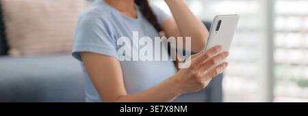 Asian adult female relaxing home using modern white cell phone for communication browsing entertainment online digital content Stock Photo