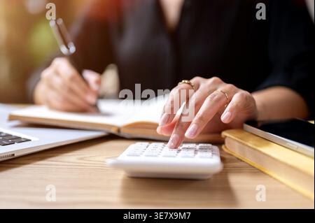 Close-up image of Thai woman's finger tapping on calculator while taking notes on table outdoor Stock Photo