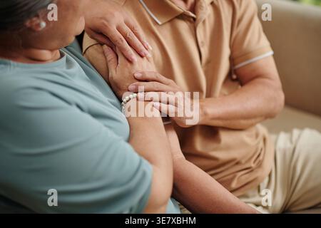 Hands of senior couple touching each other with love and tender when cuddling on couch at home Stock Photo