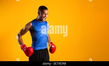 Black man wearing boxing gloves looking away while standing against yellow background in studio Stock Photo