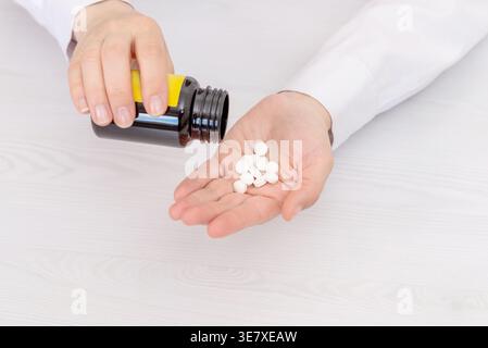 Hand pouring white tablets from bottle into palm, medication dosage and healthcare concept Stock Photo