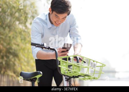 Smiling Chinese man using smartphone scanning QR code to unlock share bike outdoors Stock Photo