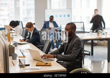 Black businessman using laptop working with business people sitting at table in office Stock Photo