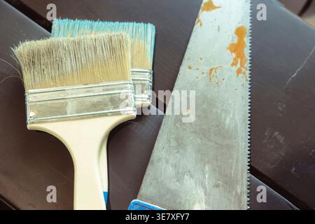 Used paint brushes and hand saw on wooden surface in indoor workspace, home renovation tools. Concept: repair process Stock Photo