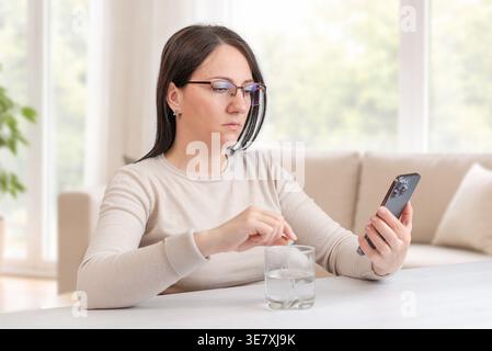 Woman checking smartphone while taking medication, concept of health tracking and routine therapy Stock Photo