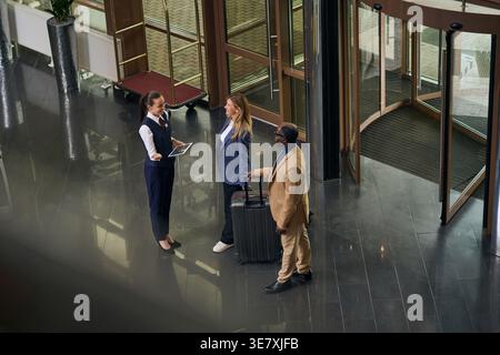 Black man and caucasian woman guest talking to female staff standing in hotel lobby Stock Photo