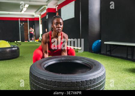 Black woman with braids doing wheel lifting exercises to strengthen quadriceps and biceps in gym Stock Photo