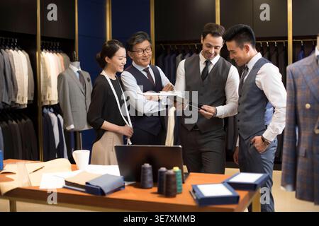 Smiling Chinese and Hispanic male and female fashion designers standing and working together in formal suits shop Stock Photo