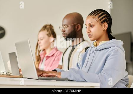 Group of programmers sitting in row at desk and working on laptops in office Stock Photo
