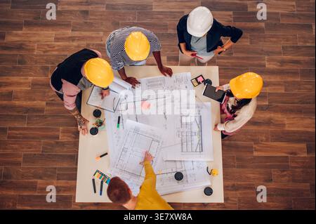 Overview Diverse group of engineers  wearing safety helmets working on blueprints on the table inside the office Stock Photo